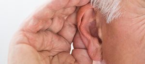 A person with hearing loss cups their hand around their ear to try and hear better.